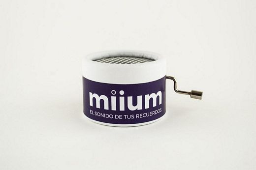 Caja redonda de color blanco con el logo de miium en fondo morado y mecanismo de manivela. Tamaño de 5cm de diámetro y 4 de altura.